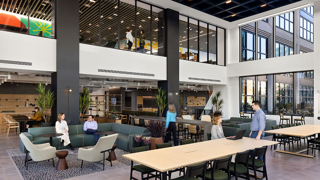 A group of people in a large room with tables and chairs.